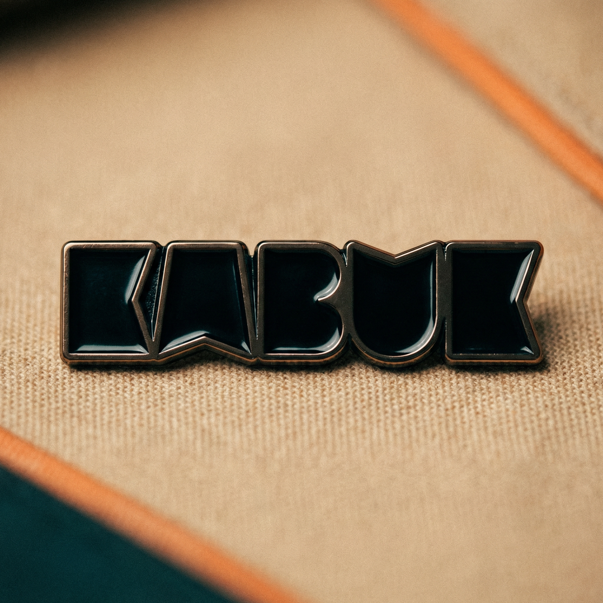 Kumaş üzerinde duran, logo formunda siyah emaye dolgulu metal pin