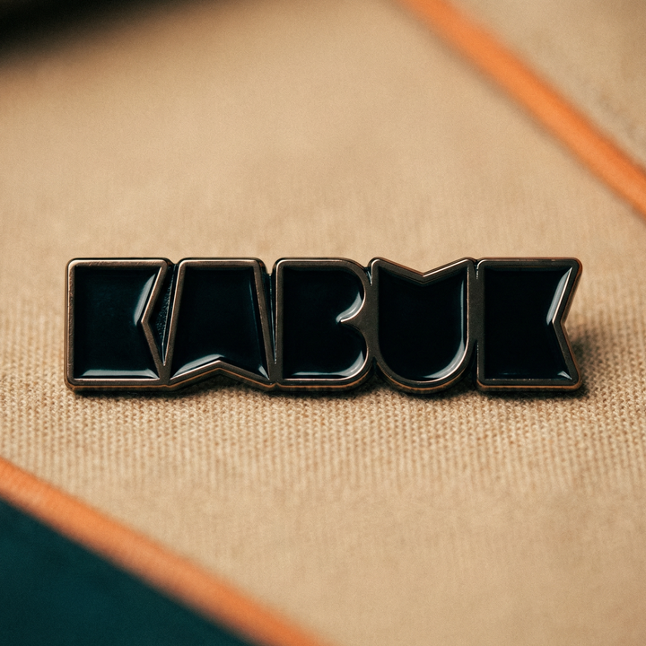 Kumaş üzerinde duran, logo formunda siyah emaye dolgulu metal pin