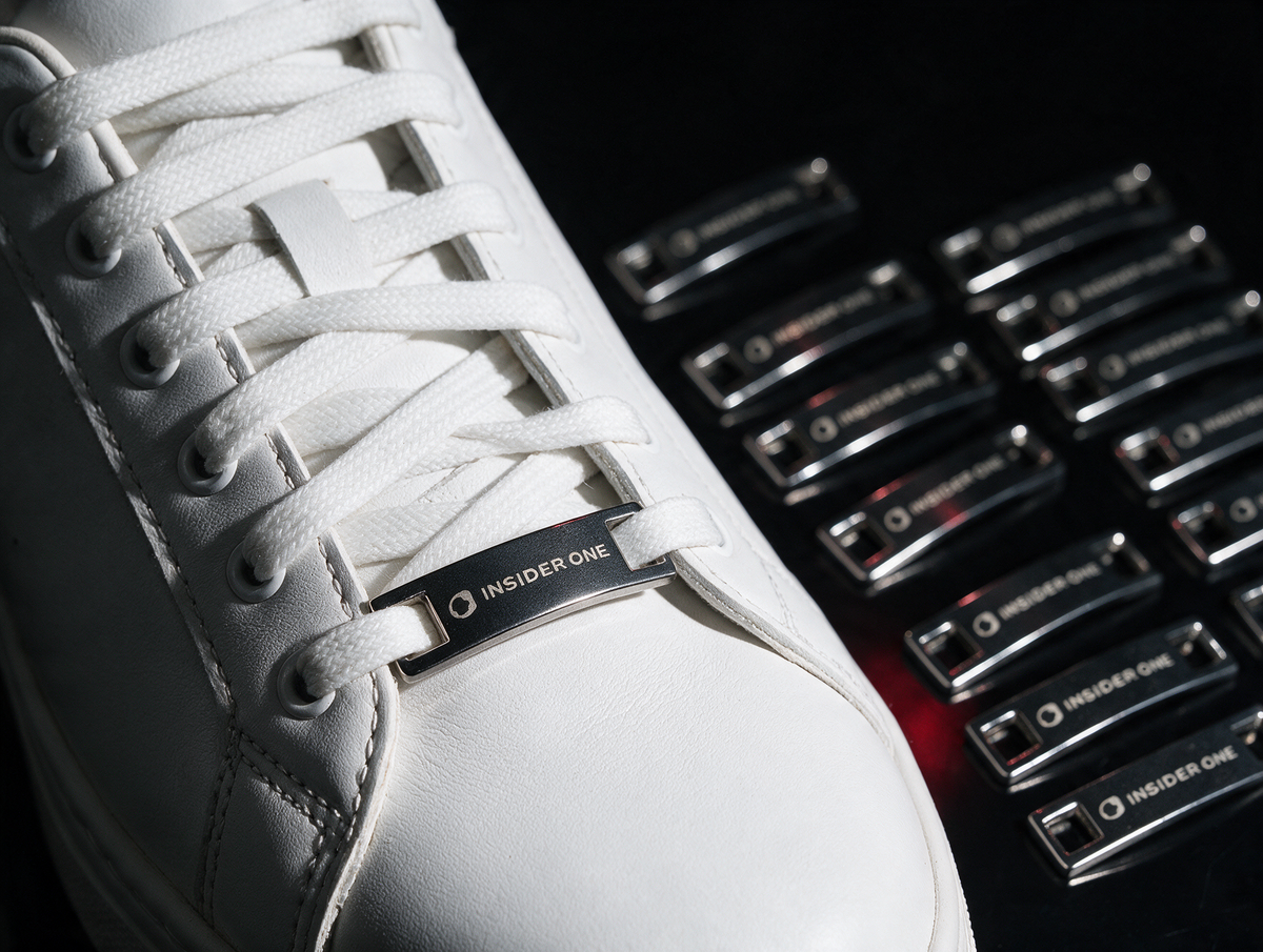 Beyaz spor ayakkabının bağcığına takılmış metal shoetag ve yanında sıralı duran shoetag'ler